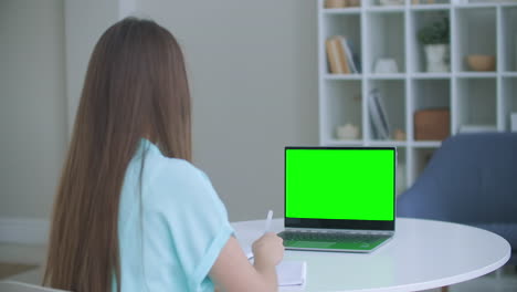 Mädchen-Macht-Sich-Notizen-Im-Notizblock-Vom-Grünen-Mockup-Bildschirm-Des-Laptop-Computers.-Mädchen-Lernt-Online-Am-Computer